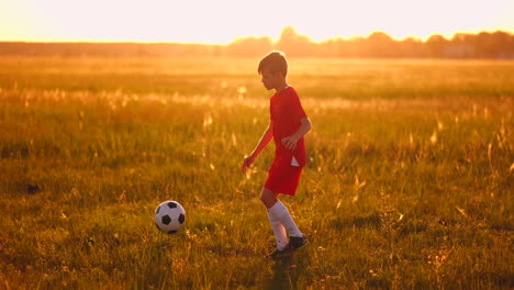 Ein-Junger-Junge-In-Einem-Roten-T-Shirt-Und-Turnschuhen-Jongliert-Bei-Sonnenuntergang-Mit-Einem-Fußball-Und-Trainiert-Und-Bereitet-Sich-Darauf-Vor,-Fußballspieler-Zu-Werden.-Der-Weg-Zum-Traum.-Harte-Arbeit